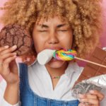 Woman with sweets—cookie, lollipop, marshmallow, chocolate—highlighting sugar addiction.
